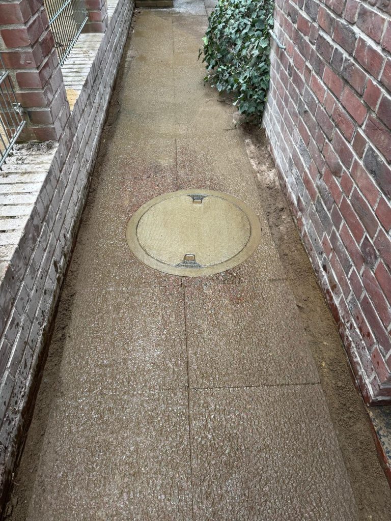 Weg mit Gullydeckel und Mauern